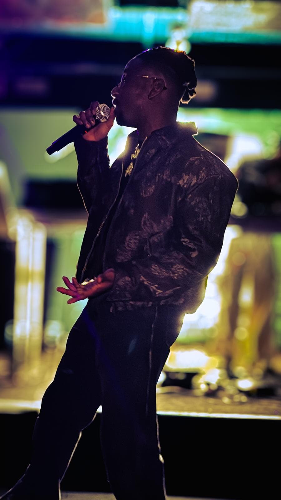 Tiyo Kay singing into a mic on stage under warm stage lights